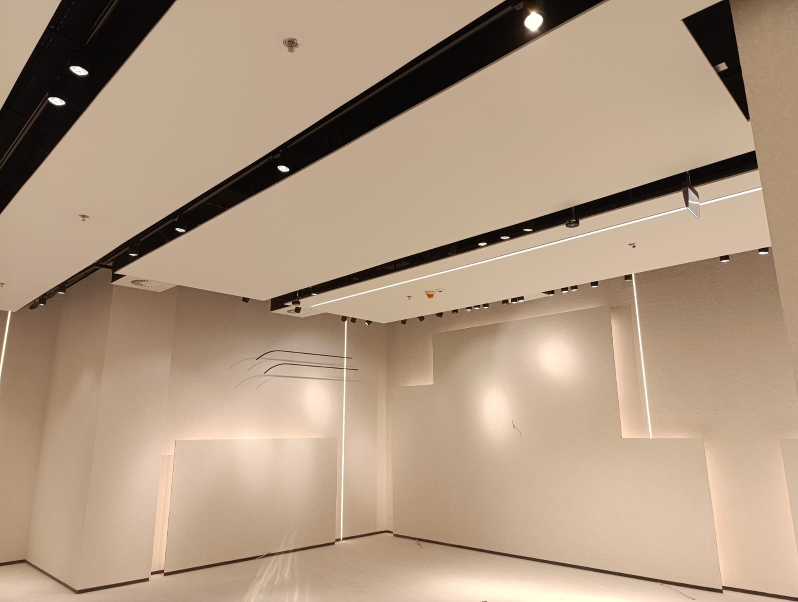 Nowoczesne oświetlenie sufitowe z czarnymi szynami i punktowymi reflektorami w jasnym wnętrzu komercyjnym. Minimalistyczny design z liniowymi lampami ściennymi.