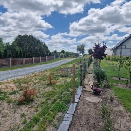 PAK PROTECT SPÓŁKA Z OGRANICZONĄ ODPOWIEDZIALNOŚCIĄ - Działka z częściowo zamontowaną siatką ogrodzeniową, widoczne słupki i podmurówka z betonowych bloczków. W tle dom i droga szutrowa.