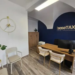 Nowoczesne biuro rachunkowe BaseTAX: minimalistyczny design, złote akcenty, drewniane biurko, eleganckie krzesła i logo na granatowej ścianie. Stylowe wnętrze.