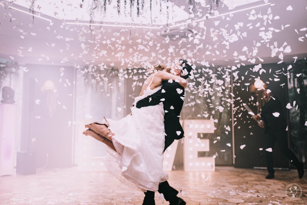 Para młoda w tańcu, zasypana konfetti w kształcie płatków, z podświetlanym napisem LOVE w tle i muzykiem z gitarą po prawej stronie.