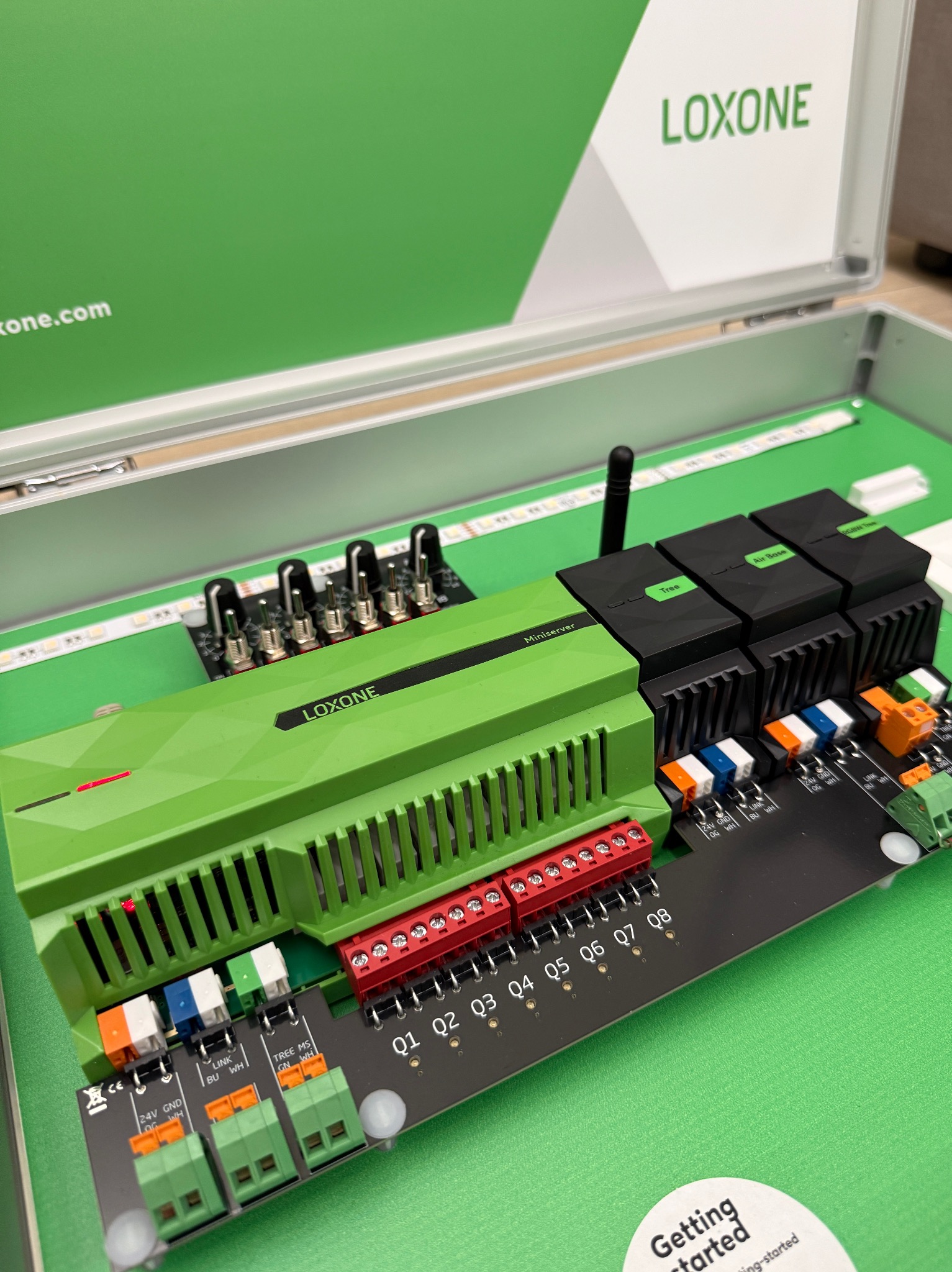 Zestaw demonstracyjny Loxone: zielony Miniserver, moduły rozszerzeń i listwa LED w aluminiowej walizce. Prezentacja systemu inteligentnego domu.