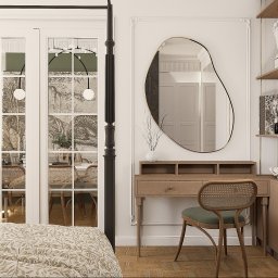 Projektant Wnętrz Studio RETRO Design - Patrycja Wawrzyniak - Elegancka toaletka z owalnym lustrem i rattanowym krzesłem, uzupełniona o półki z dekoracjami. W tle widoczne przeszklone drzwi balkonowe i wzorzysta pościel.