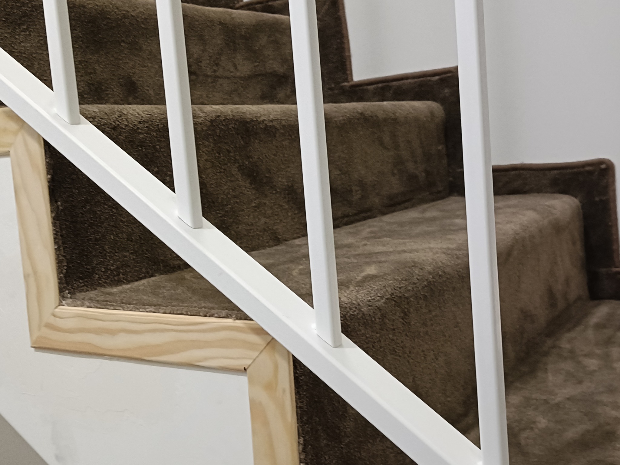 Schody wyłożone brązową wykładziną dywanową, z białymi barierkami i drewnianym wykończeniem, prezentujące detale montażu i estetyczne połączenie materiałów.
