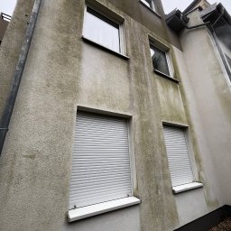 Przedsiębiorstwo Handlowo Usługowe Łukasz Muszyński - Brudna elewacja budynku z widocznymi zaciekami i zabrudzeniami, okna z roletami. Ujęcie z dołu, podkreślające pionowe zanieczyszczenia.