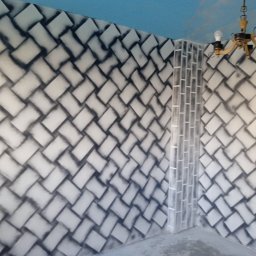 Aleksander Burkenia SPOKOBUD - Pomysłowe malowanie ścian w pokoju, imitujące plecionkę z cegieł, z efektem cieniowania. Niebieski sufit z delikatnymi obłokami i wiszący żyrandol.