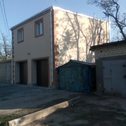 Aleksander Burkenia SPOKOBUD - Dwukondygnacyjny budynek z beżową elewacją i brązowymi detalami okien i narożników, sąsiadujący z garażami, w słoneczny dzień.