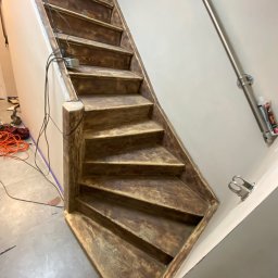 Przedsiębiorstwo wielobranżowe Emilia Senger - Drewniane schody w trakcie renowacji, widoczne ślady farby i narzędzia. Ujęcie z dołu, podkreślające strukturę drewna i etap prac wykończeniowych.