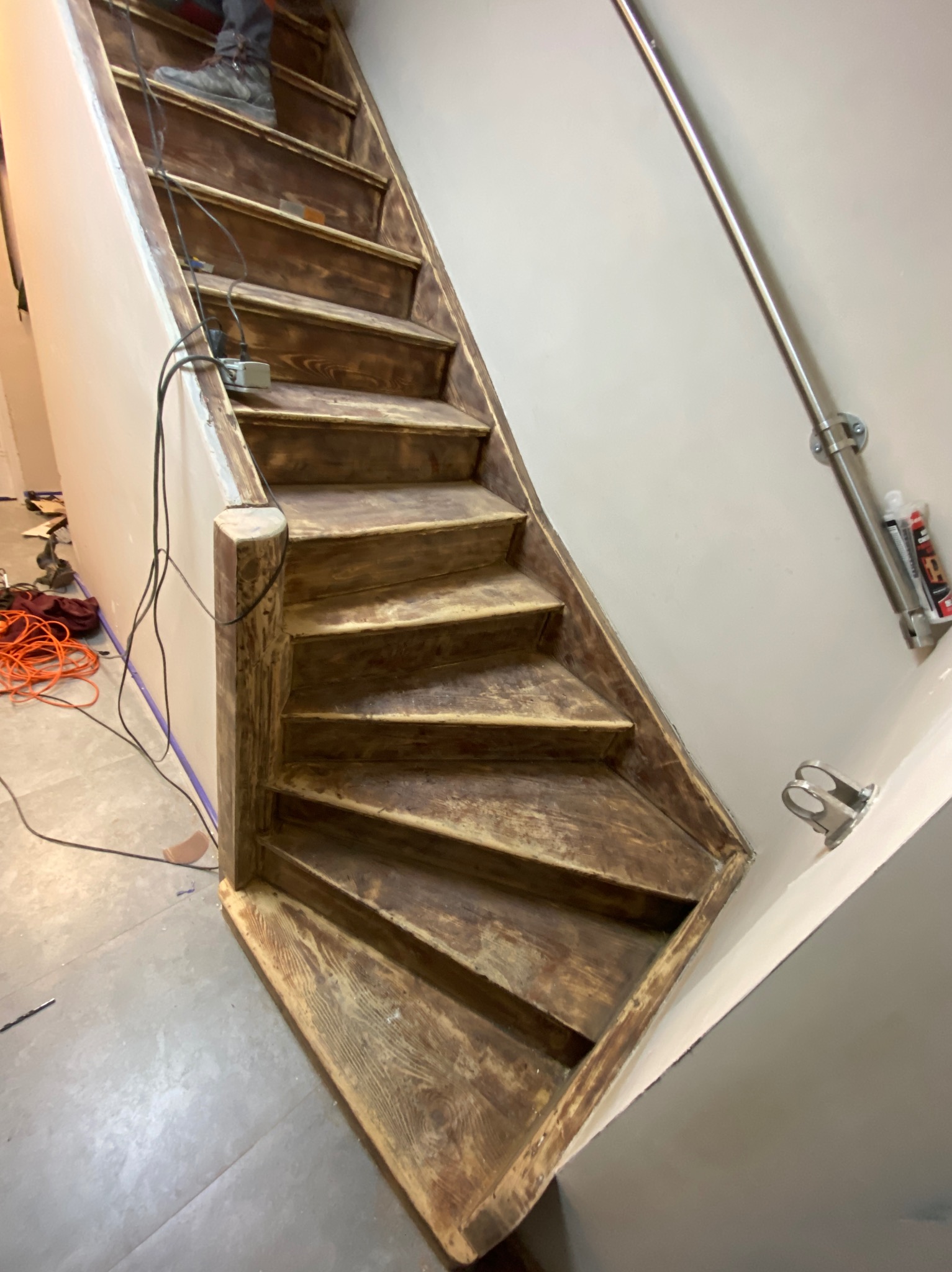 Drewniane schody w trakcie renowacji, widoczne ślady farby i narzędzia. Ujęcie z dołu, podkreślające strukturę drewna i etap prac wykończeniowych.