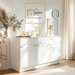 Marwex Remonty - Biała szafka łazienkowa z złotą armaturą i dekoracjami w jasnym wnętrzu, logo firmy remontowej w rogu. Minimalistyczny design, naturalne światło.
