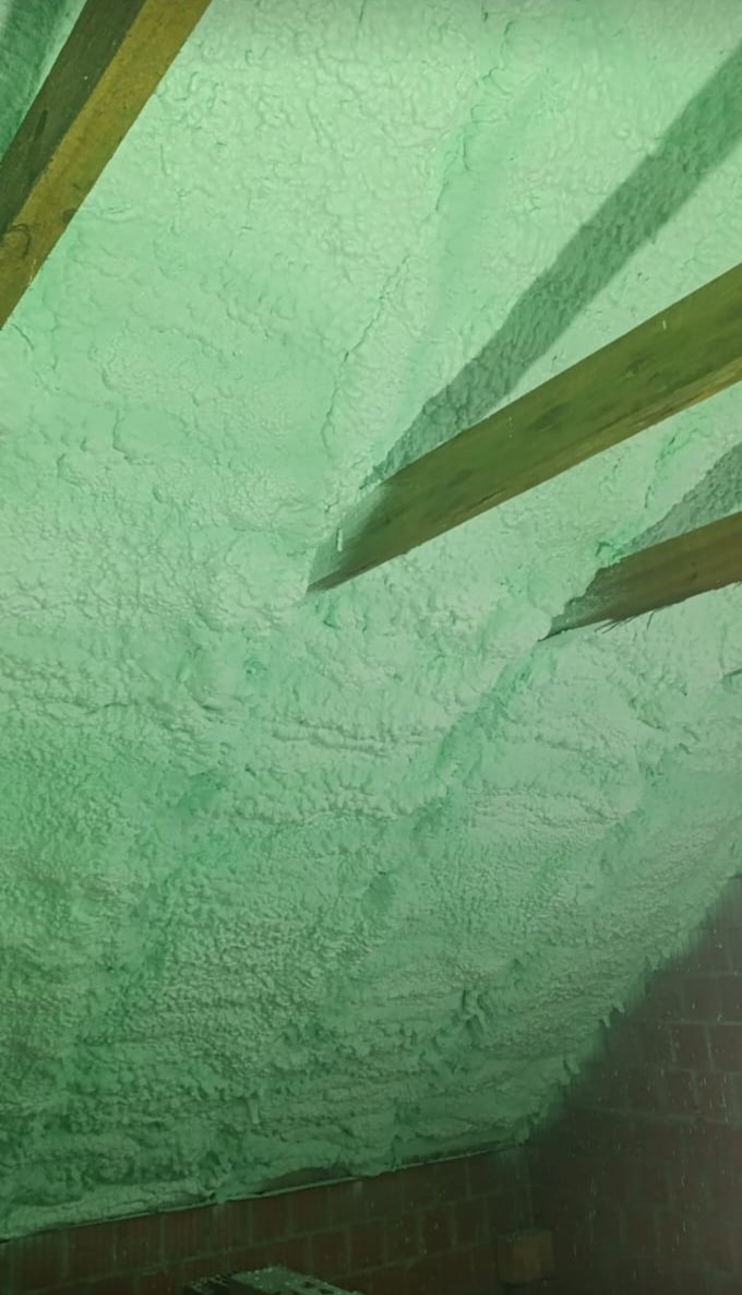 Poddasze po ociepleniu pianką PUR w Oleśnicy. Widoczne drewniane belki stropowe i struktura pianki na skośnej powierzchni dachu.