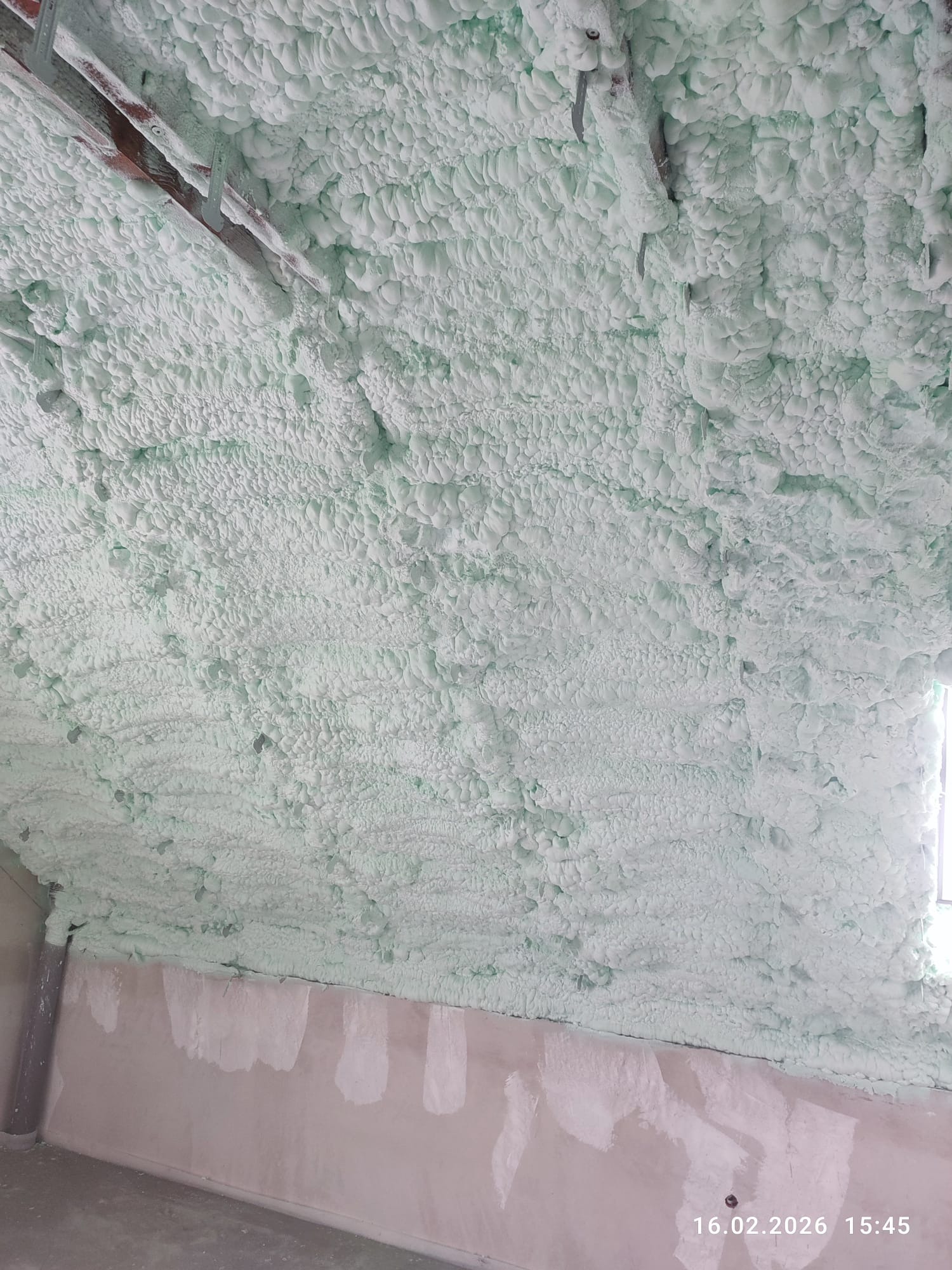 Poddasze po ociepleniu pianką PUR, widoczne drewniane elementy konstrukcyjne. Ściany częściowo przygotowane do dalszych prac wykończeniowych. Data wykonania: 16.02.2026.