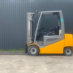 PRO LIFT Miłosz Brodzik - Żółto-szary wózek widłowy Jungheinrich EFG 530 na zewnątrz, na tle szarej ściany z blachy trapezowej. Widoczne detale konstrukcyjne i opony wózka.