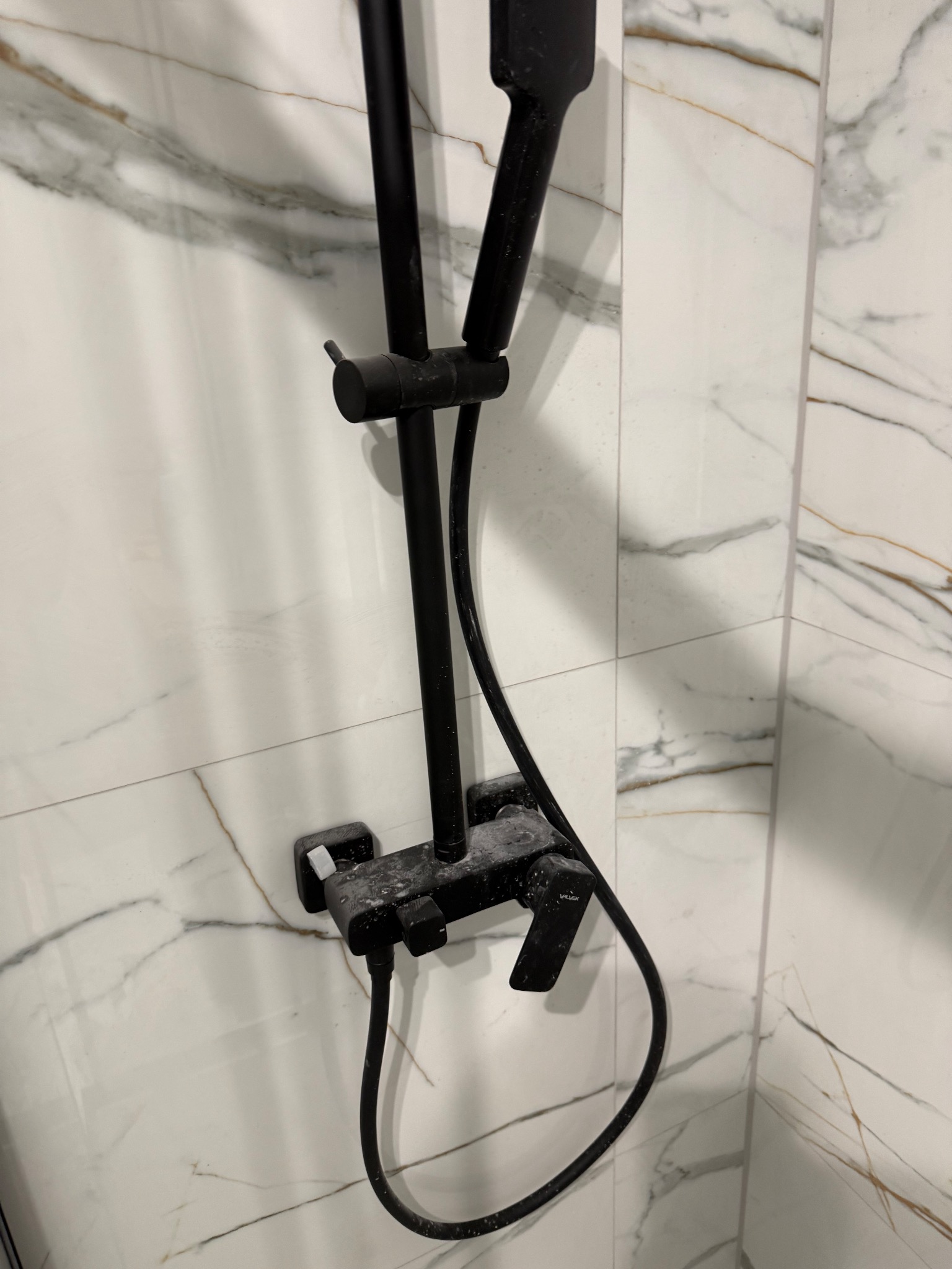 Czarny zestaw prysznicowy po czyszczeniu, widoczne ślady detergentu na armaturze i marmurowych płytkach. Ujęcie z bliska, podkreślające detale.