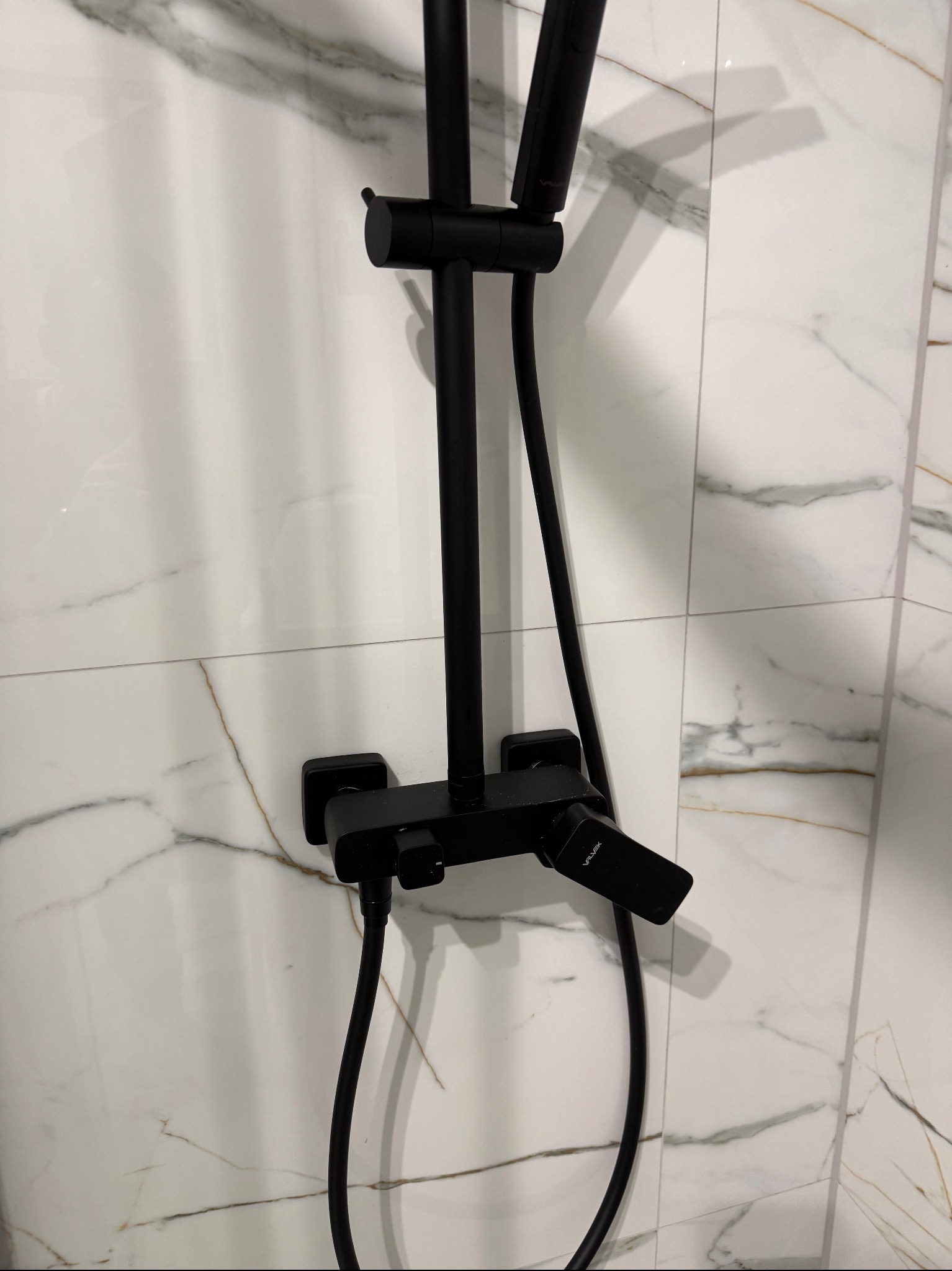 Czarny panel prysznicowy z deszczownicą na tle białych płytek imitujących marmur. Nowoczesna armatura łazienkowa po montażu, widok z bliska.