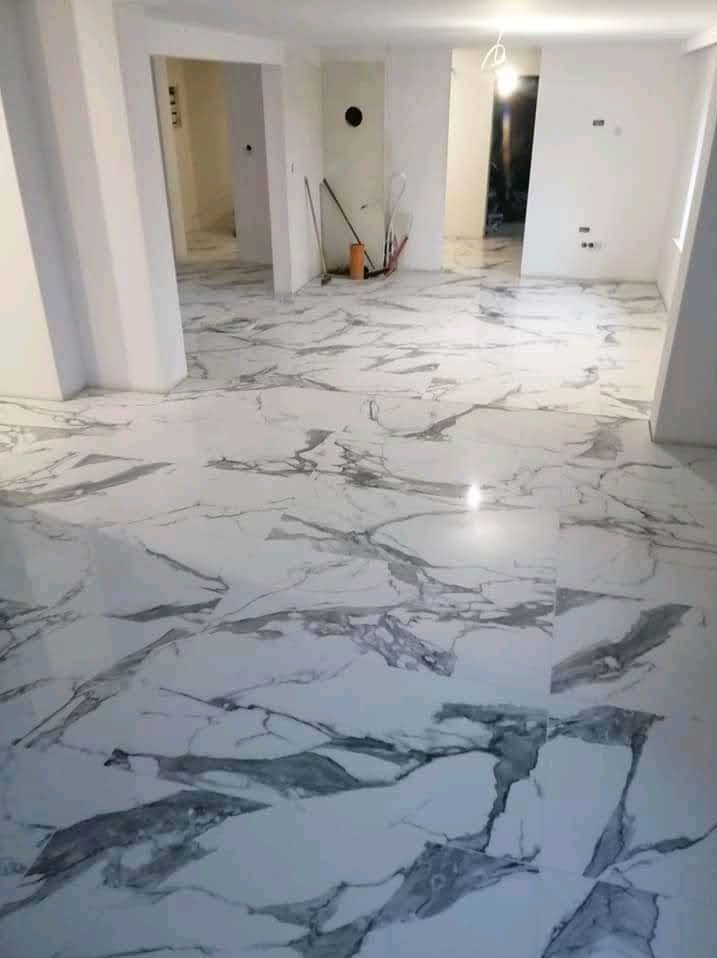 Biała marmurowa podłoga w przestronnym, jasnym wnętrzu po remoncie. Widoczne otwarte przejścia do innych pomieszczeń i narzędzia malarskie w tle.