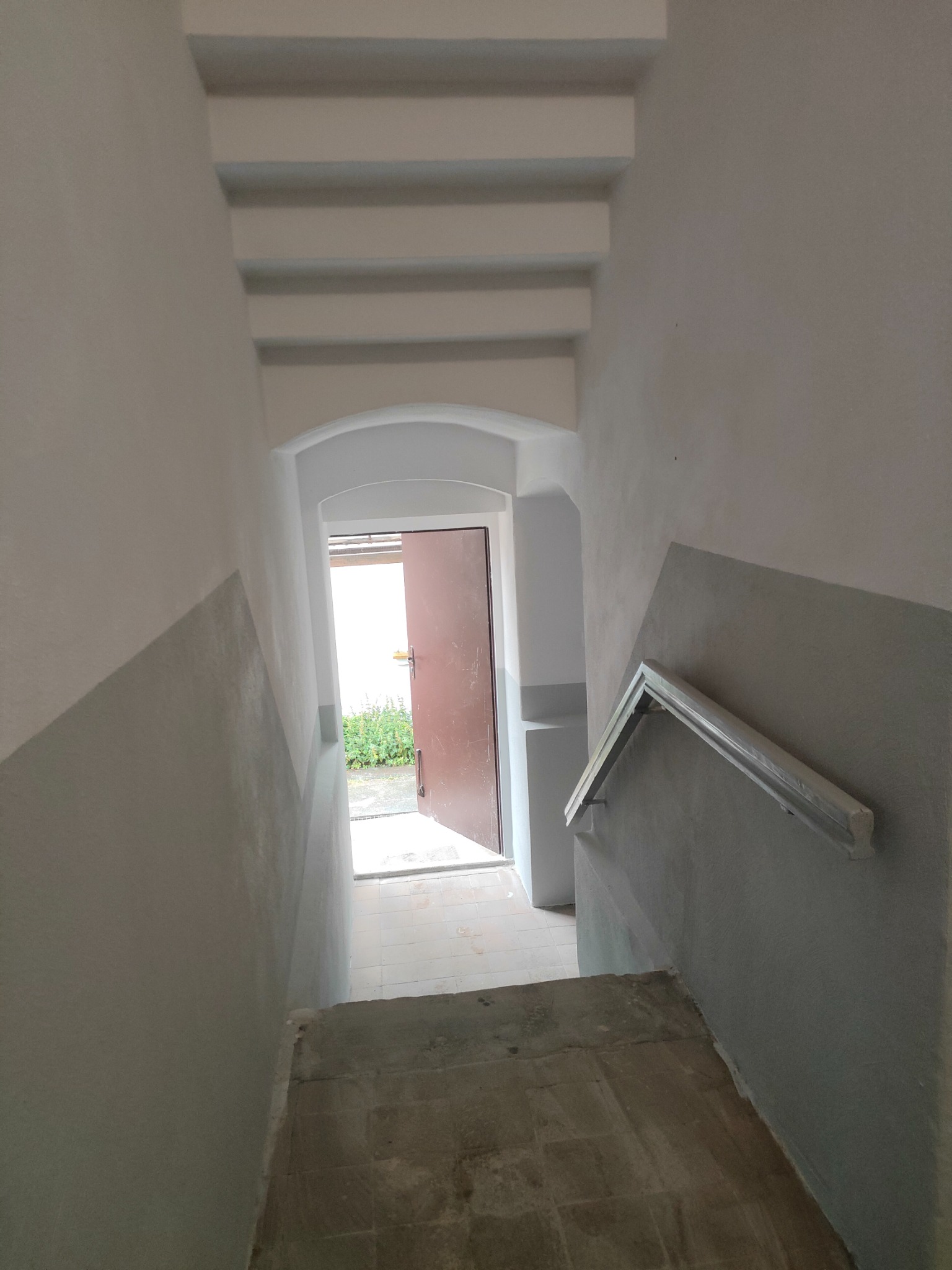 Klatka schodowa po remoncie w Lwówku Śląskim. Ściany pomalowane na szaro i biało, widoczne schody i fragment poręczy. Otwarta, brązowa  furtka na końcu schodów.