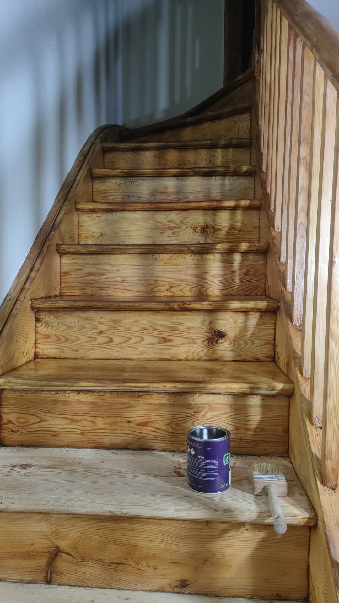 Drewniane schody po cyklinowaniu, z widoczną puszką lakieru i pędzlem na dolnym stopniu. Naturalne oświetlenie podkreśla strukturę drewna.