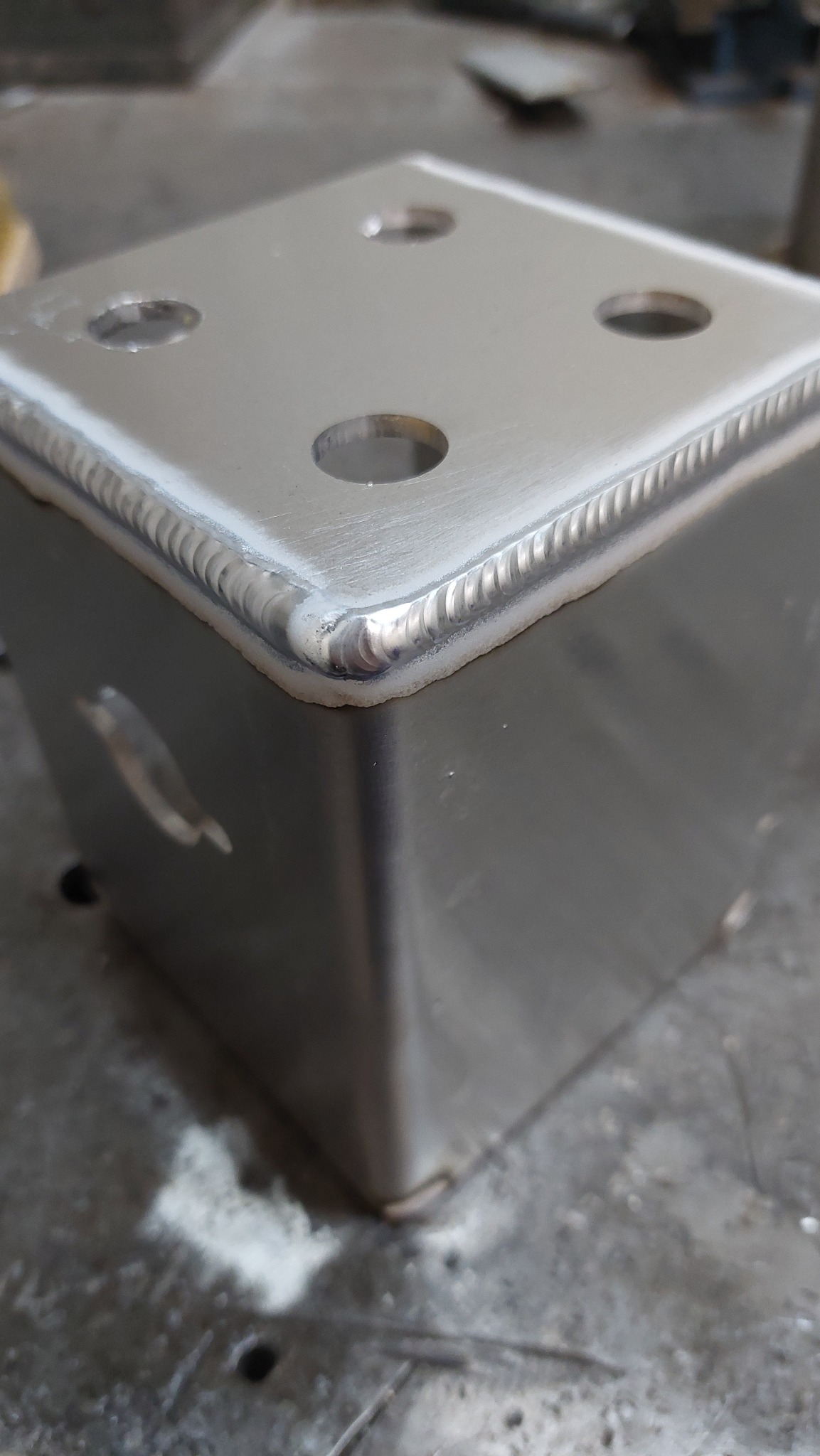 Metalowy sześcian z otworami, spawany z precyzją, widoczne ślady obróbki na powierzchni. Detal konstrukcyjny z bliska, ukazujący jakość wykonania.