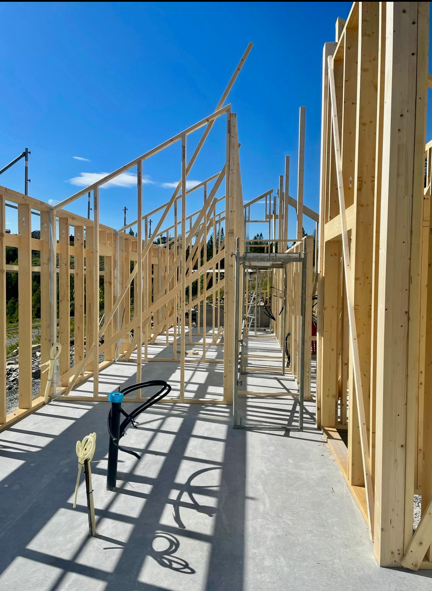 Wnętrze domu w trakcie budowy w technologii szkieletowej. Widoczne drewniane ramy konstrukcyjne, instalacje sanitarne i rusztowanie. Jasne światło słoneczne.