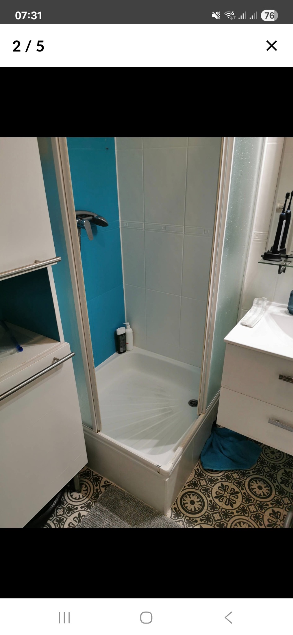 Wyremontowana łazienka z kabiną prysznicową, białą armaturą i turkusowym akcentem na ścianie. Na podłodze wzorzyste płytki. Widok na kabinę i umywalkę.