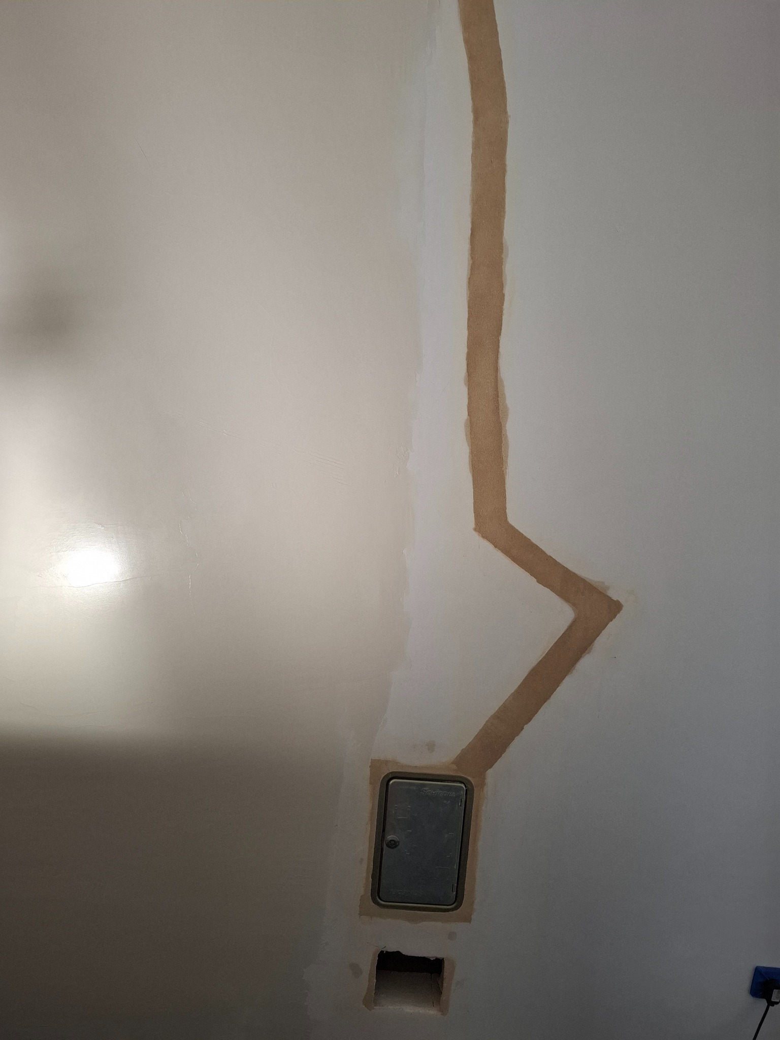 Ściana po bruzdowaniu pod instalację elektryczną, widoczna puszka elektryczna i wycięty otwór. Przygotowanie do malowania.