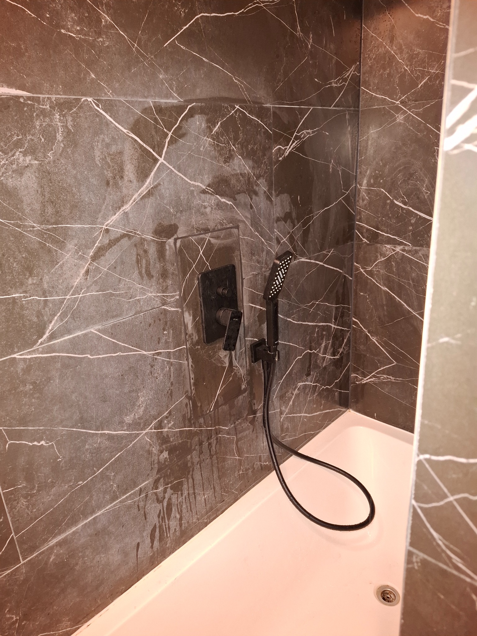 Nowoczesna kabina prysznicowa z czarną armaturą i płytkami imitującymi marmur. Minimalistyczny design, eleganckie wykończenie.