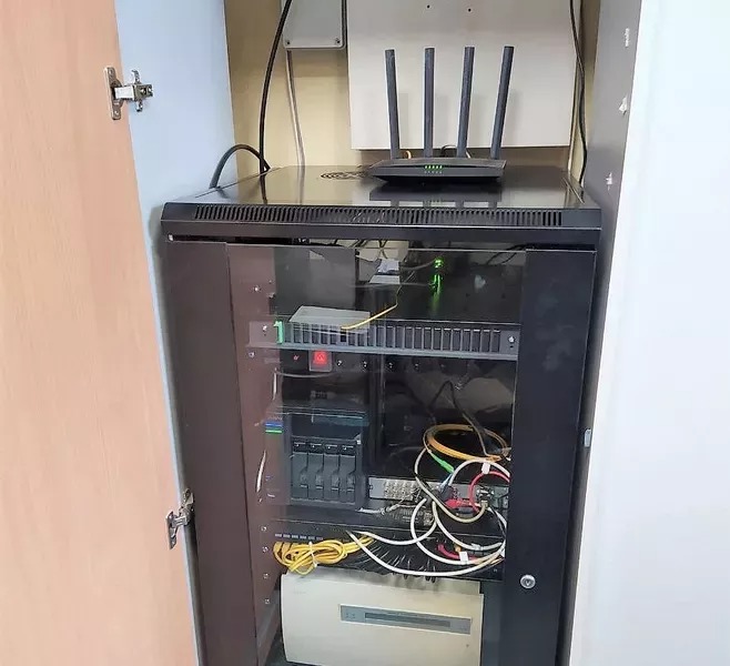 Szafa rack z routerem i okablowaniem sieciowym w szafie wnękowej z uchylonymi drzwiami, widok z bliska na zainstalowany sprzęt.