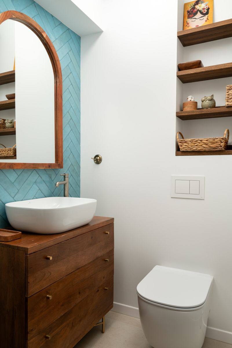 Nowoczesna łazienka z umywalką nablatową na drewnianej komodzie, błękitnymi płytkami w jodełkę i drewnianymi półkami w ścianie. Minimalistyczny design.