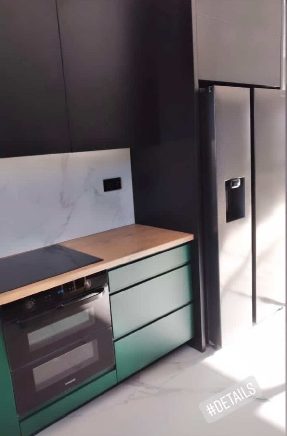 Nowoczesna kuchnia we Wrocławiu: czarne szafki górne, zielone dolne, drewniany blat i marmurowa ściana. Minimalistyczny design z lodówką side-by-side.