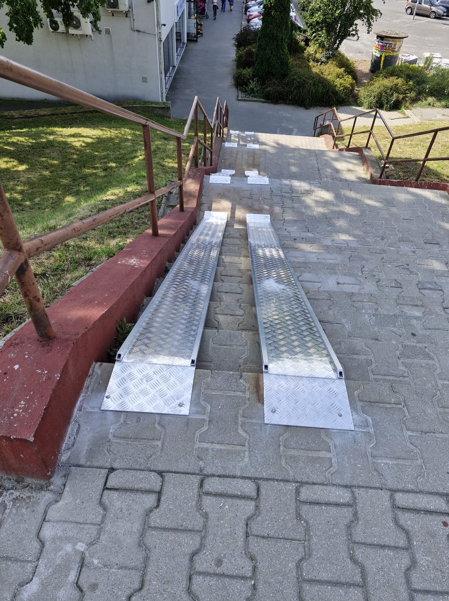 Metalowe najazdy dla wózków inwalidzkich na schodach z kostki brukowej w Jastrzębiu-Zdroju. Ułatwienie dostępu dla osób z niepełnosprawnościami, widok z góry.