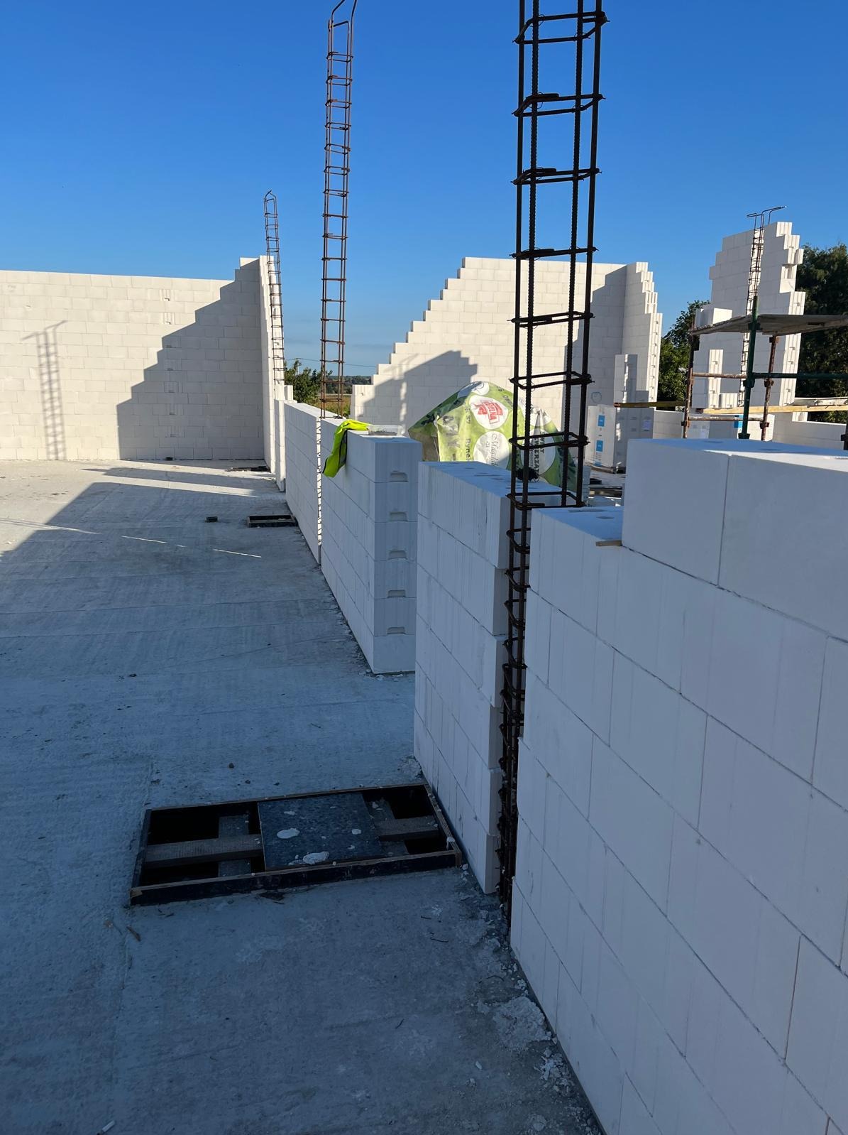 Wznoszenie ścian z betonu komórkowego Ytong. Widoczne zbrojenia pionowe i fragmenty ścian o schodkowej strukturze. Na pierwszym planie otwór w stropie.