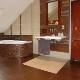 ARTUR ŁACH GLAZAR - Nowoczesna łazienka na poddaszu z brązowymi płytkami, wanną obudowaną mozaiką, umywalką i wysoką szafką. Uwagę zwraca okno dachowe wpuszczające naturalne światło.