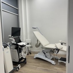 MW Medic - Medycyna Estetyczna Warszawa - Jasne wnętrze gabinetu lekarskiego z nowoczesnym sprzętem, białym fotelem zabiegowym i drewnianą podłogą. Widok zza uchylonych drzwi.