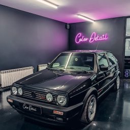 COLOR DETAIL SPÓŁKA Z OGRANICZONĄ ODPOWIEDZIALNOŚCIĄ - Czarny, lśniący Volkswagen Golf GTI Mk2 po detailingu, z neonem 'Color Detail' w tle. Błyszcząca podłoga odbija światło, podkreślając efekt.