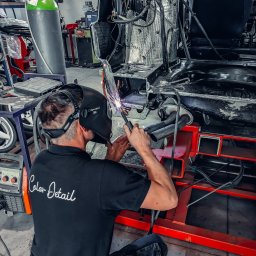 COLOR DETAIL SPÓŁKA Z OGRANICZONĄ ODPOWIEDZIALNOŚCIĄ - Spawanie karoserii auta w warsztacie. Mężczyzna w masce spawalniczej 3M łączy elementy konstrukcyjne. Widoczny spawacz, spawarka Kempack i butla z gazem.