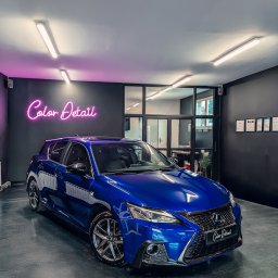 COLOR DETAIL SPÓŁKA Z OGRANICZONĄ ODPOWIEDZIALNOŚCIĄ - Błyszczący, niebieski Lexus CT w studiu detailingowym z neonem 'Color Detail' na ścianie. Widoczne certyfikaty na ścianie i odbicia w lakierze.