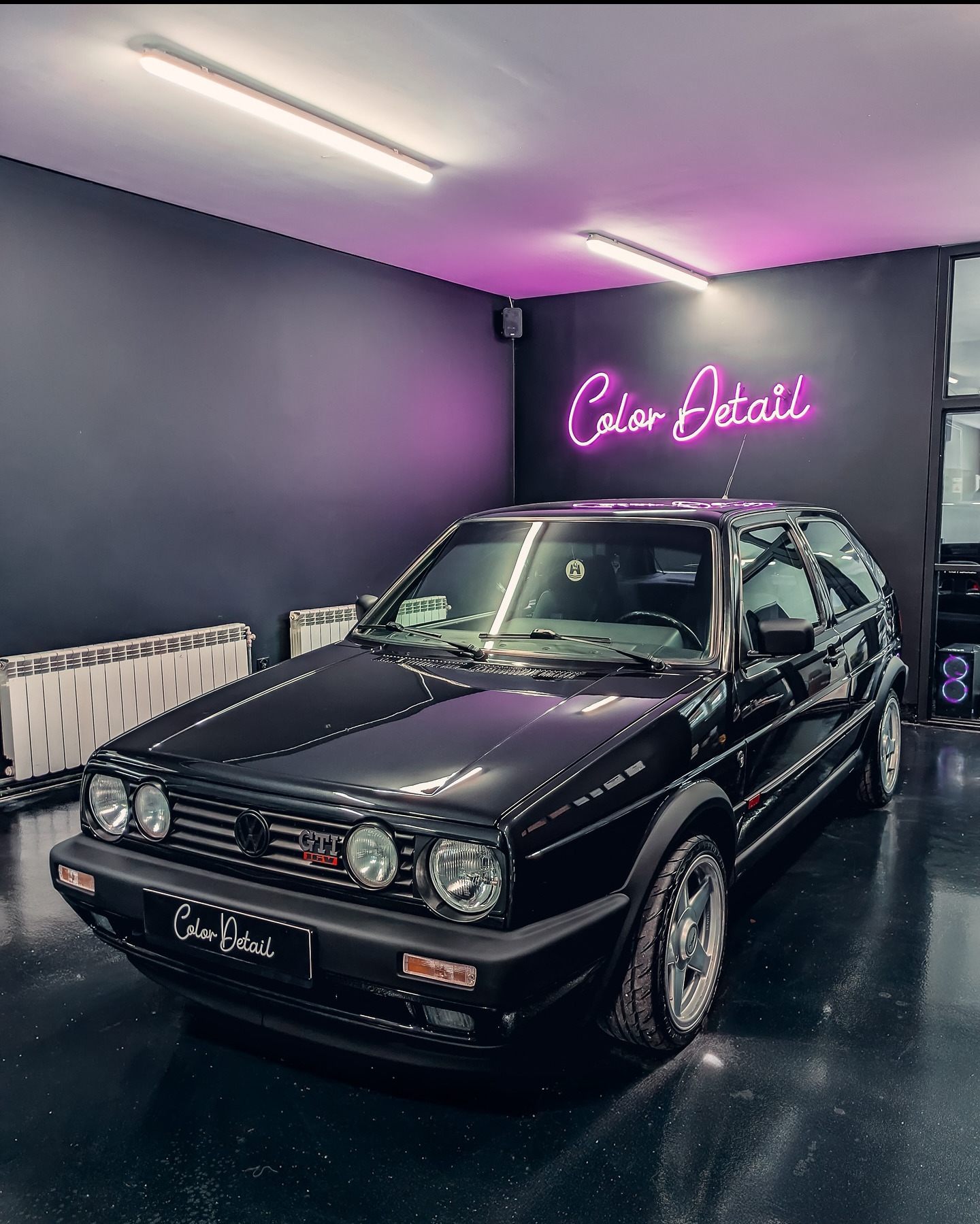 Czarny, lśniący Volkswagen Golf GTI Mk2 po detailingu, z neonem 'Color Detail' w tle. Błyszcząca podłoga odbija światło, podkreślając efekt.