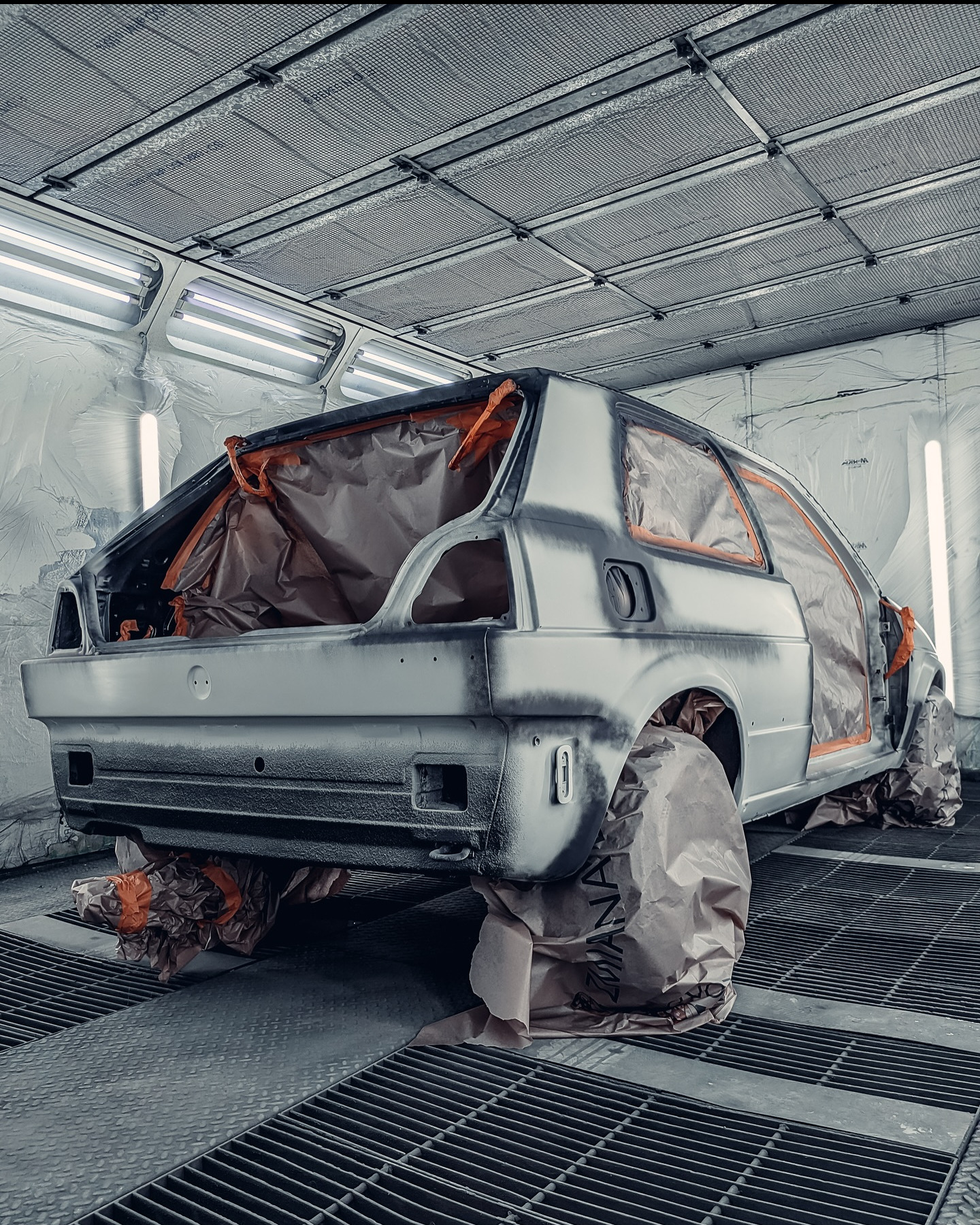 Przygotowanie do lakierowania: szary samochód z maskowaniem w kabinie lakierniczej w Bożej Woli. Widok z tyłu, oświetlenie jarzeniowe, kratka podłogowa.