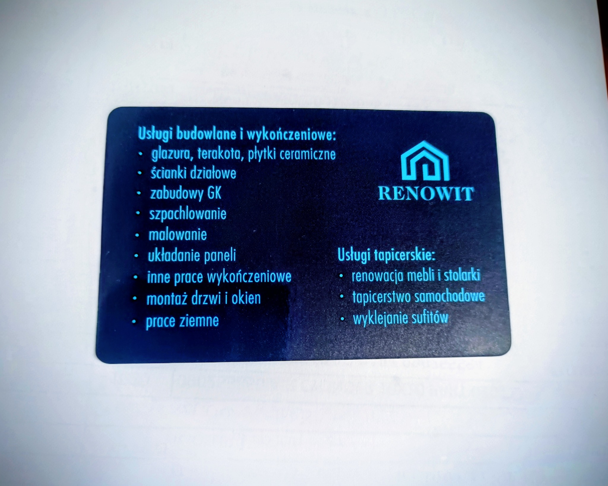 Wizytówka firmy Renowit oferującej usługi budowlane, wykończeniowe i tapicerskie, z wyliczeniem zakresu prac. Ciemne tło, jasny tekst, logo w kształcie domu.