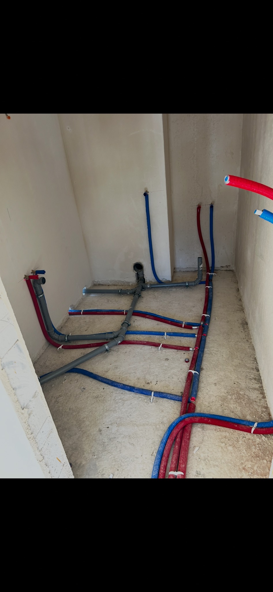 Szare i kolorowe rury instalacji wodnej i kanalizacyjnej w surowym pomieszczeniu, widok z góry. Rury połączone z zaworem i odpływem.