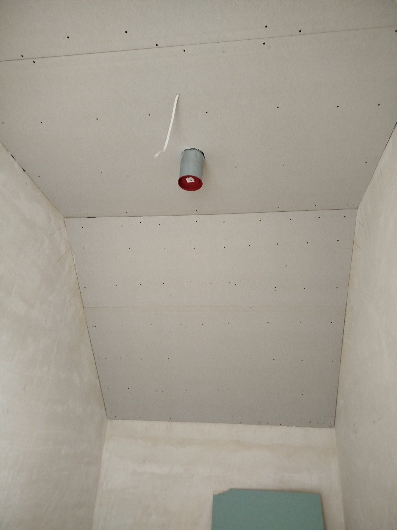 Zamontowana płyta karton-gips na suficie poddasza z widocznym otworem wentylacyjnym i wystającym kablem. Ściany w surowym stanie, przygotowane do dalszych prac.