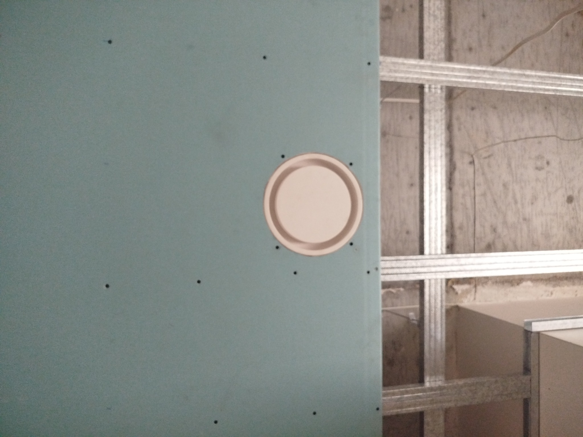 Niebieska płyta karton-gips z wyciętym otworem na puszkę elektryczną, widoczna metalowa konstrukcja nośna. Ślady po wkrętach na płycie.