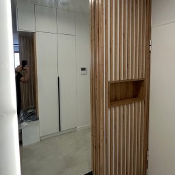 Fusion Furniture ANTON FIHURKA - Nowoczesny przedpokój z lustrem z podświetleniem LED i drewnianą ścianką działową z wnęką, odbicie szafy w lustrze, jasna podłoga.