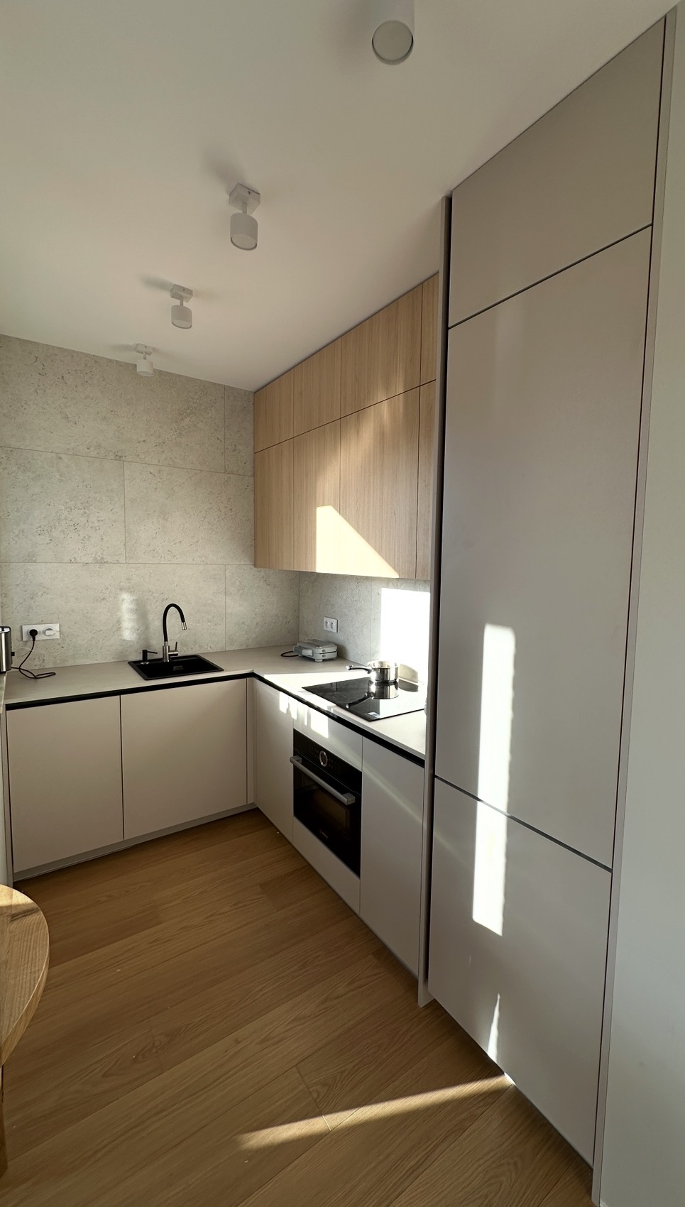 Jasna kuchnia w stylu skandynawskim z drewnianymi i białymi szafkami, czarnym zlewem i płytą indukcyjną. Na blacie stoi garnek, a na podłodze widać drewniane panele.