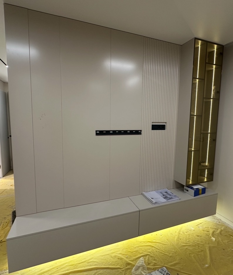 Biała zabudowa meblowa z podświetleniem LED i dekoracyjnym panelem ściennym. Nowoczesny design, minimalistyczny styl. Widoczne materiały wykończeniowe na podłodze.