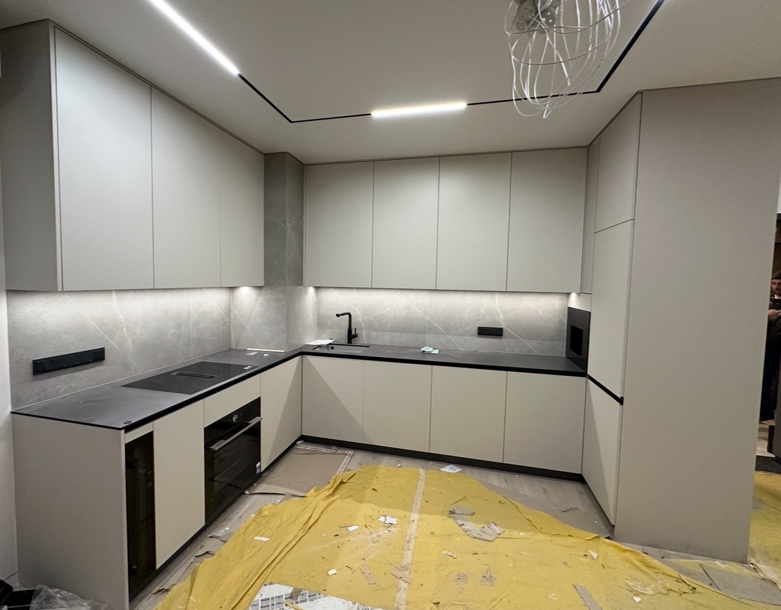 Nowoczesna, jasna kuchnia z szarymi frontami i czarnymi akcentami. Widoczne oświetlenie LED podszafkowe i sufitowe. Podłoga zabezpieczona folią malarską.