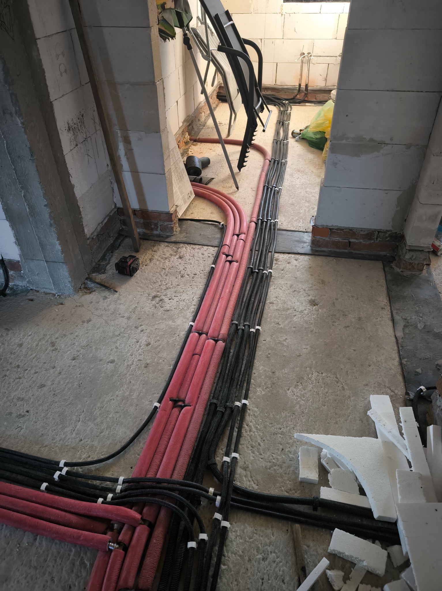 Równolegle ułożone kable elektryczne w peszlach, częściowo czerwonych i czarnych, prowadzone wzdłuż surowej ściany z betonu komórkowego w trakcie remontu.