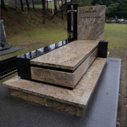 Moczadło Tomasz Zakład kamieniarski - Granitowy nagrobek z krzyżem i tablicą pamiątkową na cmentarzu, wykonany z kamienia w odcieniach beżu i czerni, z widoczną datą urodzin i śmierci.