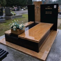 Moczadło Tomasz Zakład kamieniarski - Granitowy nagrobek z jasnego kamienia z krzyżem i czarnymi elementami, na cmentarzu. Na pomniku kwiaty w kamiennej donicy. Widoczne dane osoby zmarłej.