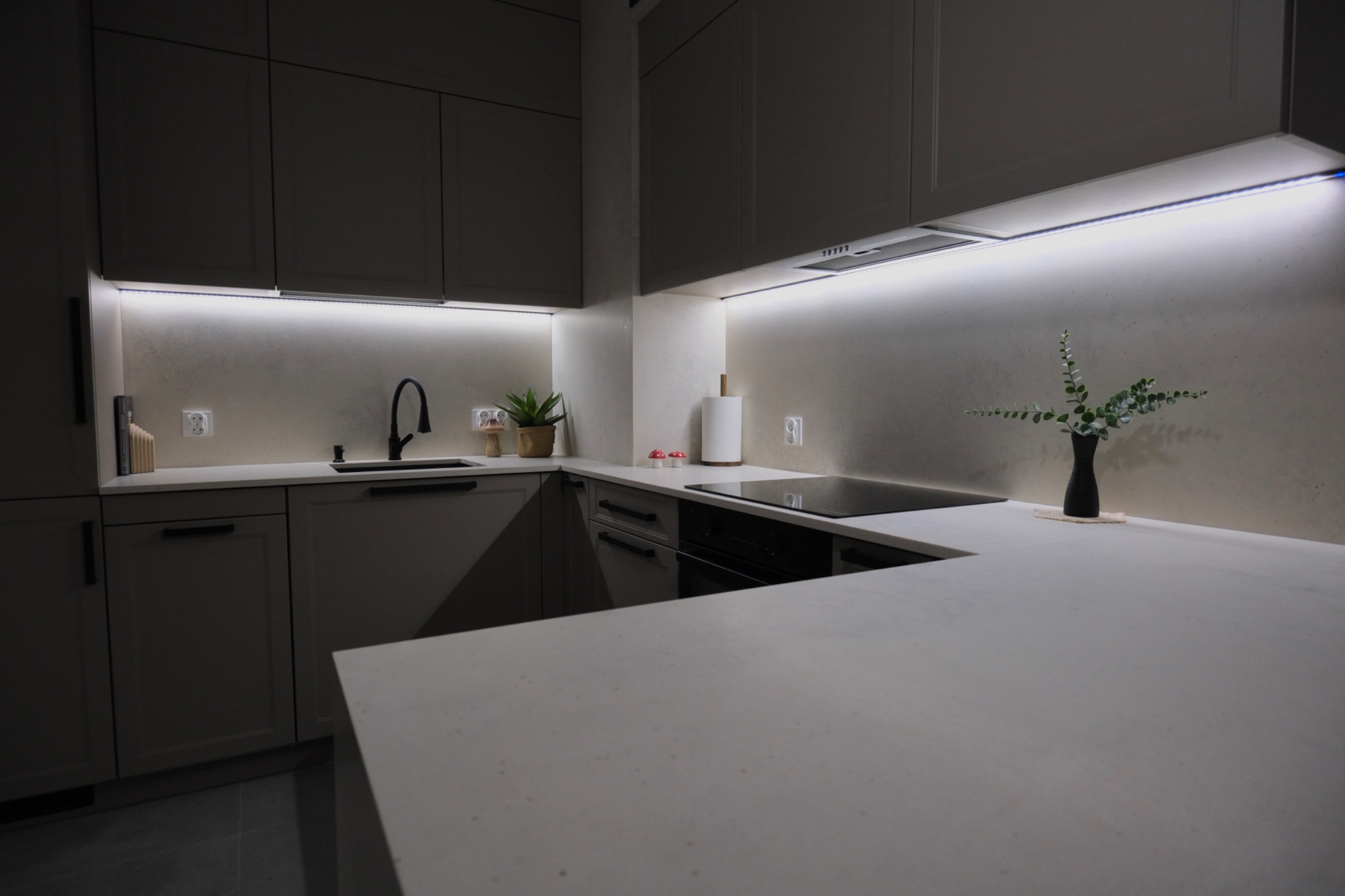 Nowoczesna kuchnia z blatem w odcieniach szarości, oświetleniem LED pod szafkami i minimalistycznym wystrojem. Ujęcie z niskiego kąta podkreśla przestronność.